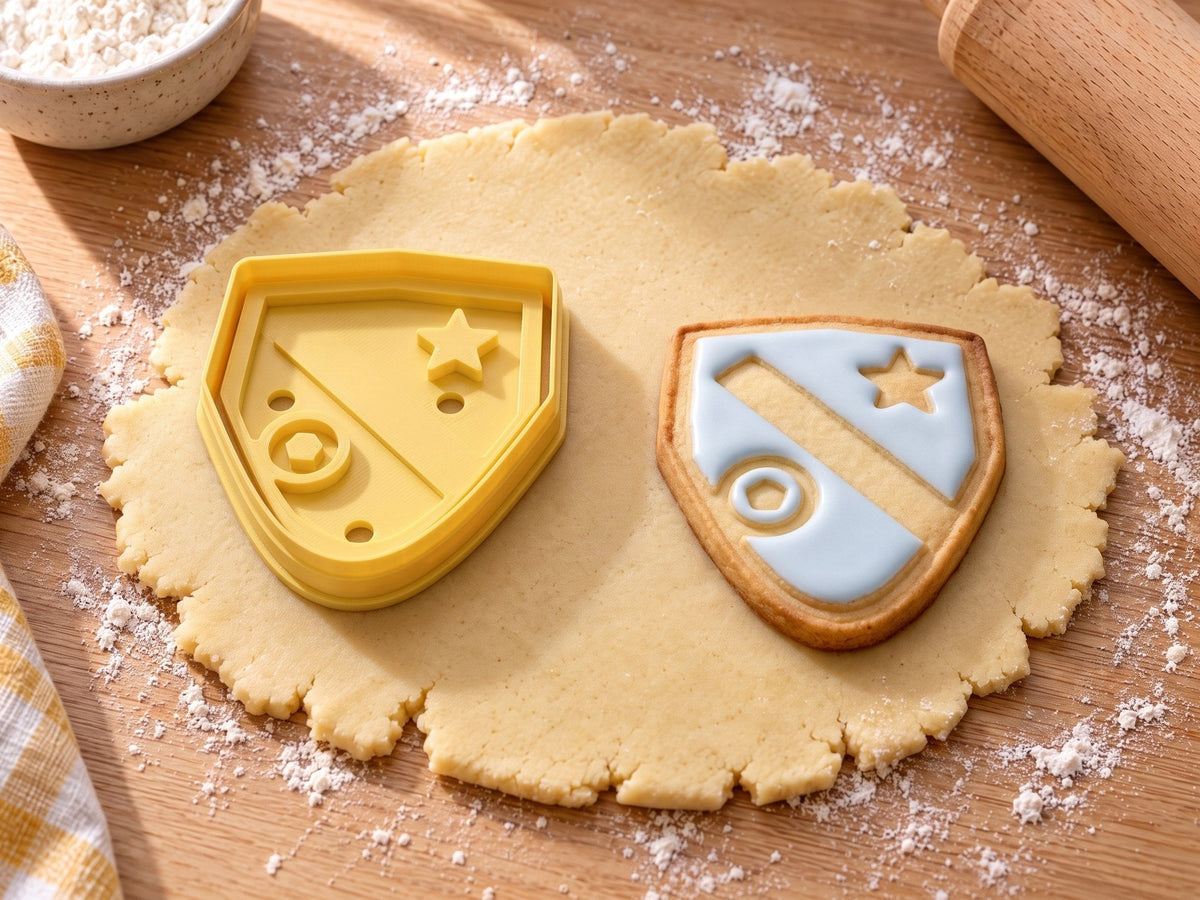 Wappen-Ausstecher mit Prägung neben einem gebackenen Wappenkeks mit hellblauem Zuckerguss, Schrägbalken, Stern und Ball auf ausgerolltem Teig