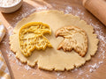 Butter-gelber Adlerkopf-Ausstecher mit Prägung neben gebackenem Keks mit Hakenschnabel und gezacktem Federkragen auf hellem Holz