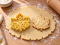 Butter-gelber Ahornblatt-Ausstecher mit Prägung neben gebackenem Keks mit fein verästelten Blattadern auf hellem Holz