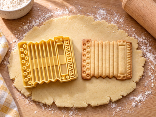 Butter-gelber Akkordeon-Ausstecher mit Prägung neben gebackenem Keks mit Bassknöpfen, Faltenbalg und Tasten auf hellem Holz
