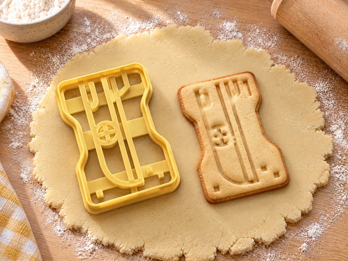 Butter-gelber Anspitzer-Ausstecher mit Prägung neben gebackenem Keks mit Klinge und Kreuzschraube auf hellem Holz