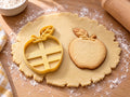 Butter-gelber Apfel-Ausstecher mit Prägung neben gebackenem Keks mit Stiel und geädertem Blatt auf hellem Holz