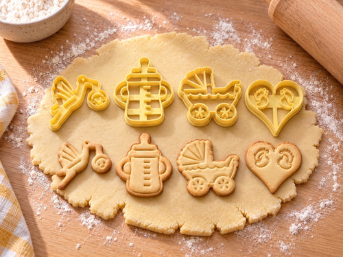 Set Baby & Taufe: 4 butter-gelbe Ausstecher mit Prägung nebeneinander mit gebackenen, geprägten Keksen auf ausgerolltem Teig und hellem Holz
