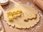 Butter-gelber Ausstecher mit Prägung als Wäscheleine neben gebackenem Keks mit Strampler, Hemdchen und Söckchen auf hellem Holz