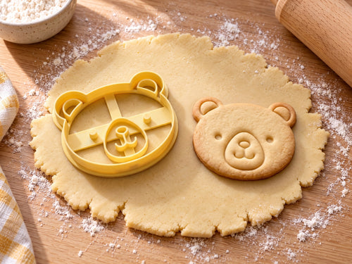 Butter-gelber Bärenkopf-Ausstecher mit Prägung neben gebackenem Keks mit runden Ohren, Punktaugen und Schnäuzchen auf hellem Holz