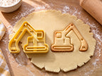 Butter-gelber Bagger-Ausstecher mit Prägung neben gebackenem Bagger-Keks mit Kettenlaufwerk und Schaufel auf hellem Holz