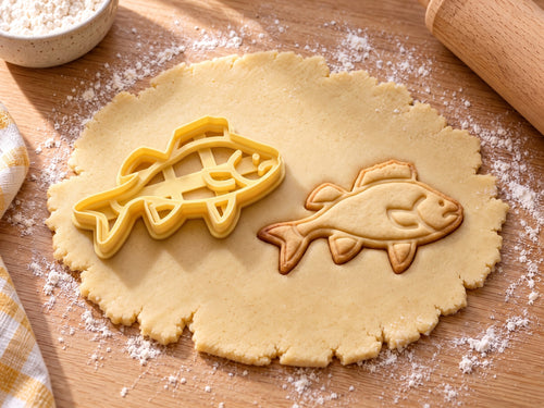 Butter-gelber Barsch-Ausstecher mit Prägung neben gebackenem Keks mit Rückenflosse, Kiemen und Bauchflossen auf hellem Holz