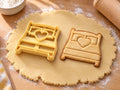 Butter-gelber Bett-Ausstecher mit Prägung neben Keks mit Doppelbett, zwei Kissen und Herz auf hellem Holz