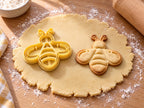 Butter-gelber Bienen-Ausstecher mit Prägung neben gebackenem Keks mit symmetrischer Biene, drei Streifen und zwei Flügeln auf hellem Holz