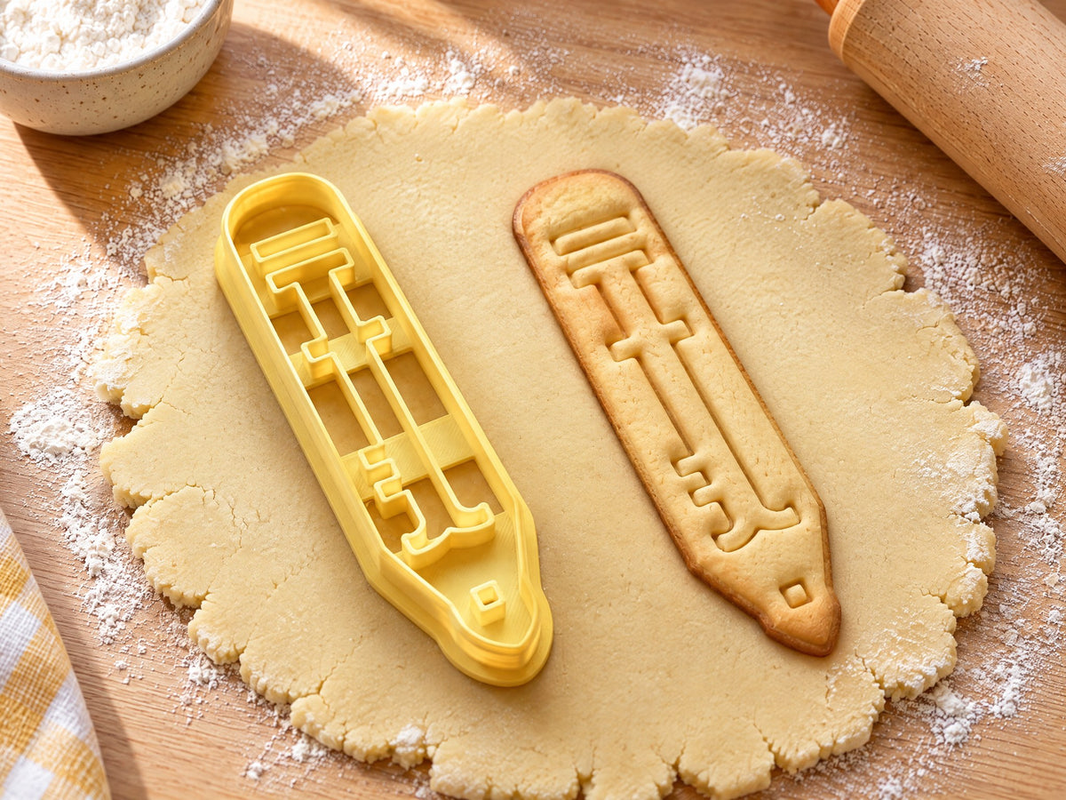 Butter-gelber Bleistift-Ausstecher mit Prägung neben schmalem gebackenem Keks mit Radiergummi und gespitzter Mine auf hellem Holz