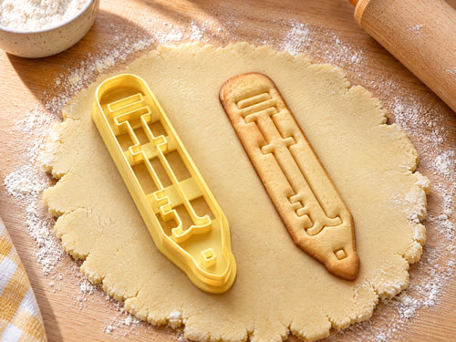 Butter-gelber Bleistift-Ausstecher mit Prägung neben schmalem gebackenem Keks mit Radiergummi und gespitzter Mine auf hellem Holz