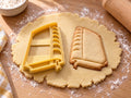 Butter-gelber Buch-Ausstecher mit Prägung neben gebackenem Keks mit gewölbtem Buchrücken und Lesezeichen auf hellem Holz