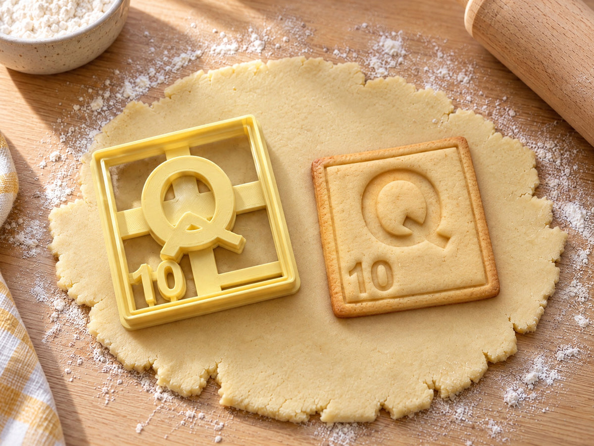 Butter-gelber Ausstecher Buchstabe Q mit Prägung neben quadratischem Keks mit kräftigem Q und Punktwert 10 auf hellem Holz