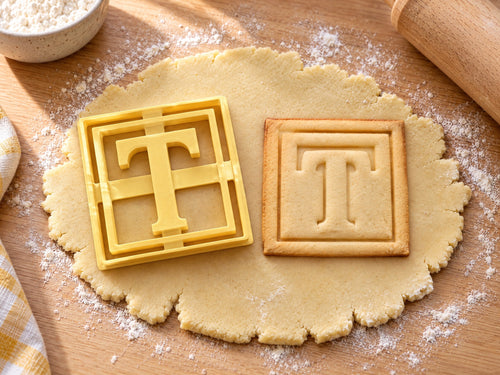 Butter-gelber Ausstecher Buchstabe T mit Prägung neben quadratischem Keks mit Serifen-T im doppelten Rahmen auf hellem Holz