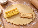Butter-gelber Bus-Ausstecher mit Prägung neben gebackenem Bus-Keks mit fünf Fenstern und Doppeltür auf hellem Holz