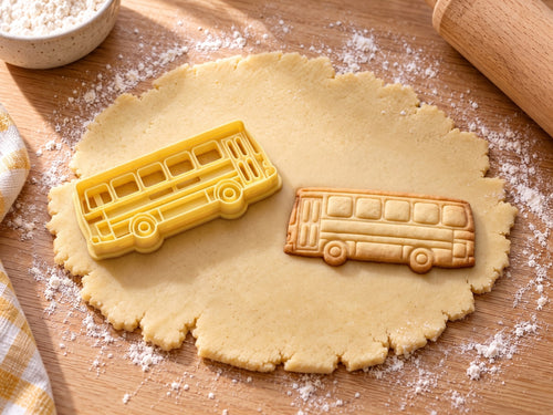 Butter-gelber Bus-Ausstecher mit Prägung neben gebackenem Bus-Keks mit fünf Fenstern und Doppeltür auf hellem Holz