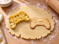 Butter-gelber Gamepad-Ausstecher mit Prägung neben gebackenem Keks mit Mittelfeld, Steuerkreuz und vier Tasten auf hellem Holz
