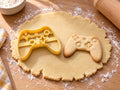 Butter-gelber Gamepad-Ausstecher mit Prägung neben gebackenem Keks mit Steuerkreuz in der Mitte und runden Tasten auf hellem Holz