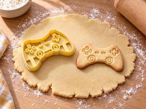 Butter-gelber Controller-Ausstecher mit Prägung neben gebackenem Keks mit Steuerkreuz oben rechts und zwei Sticks auf hellem Holz
