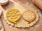 Butter-gelber Dartscheiben-Ausstecher mit Prägung neben rundem gebackenem Keks mit Ringen, Feldern und Pfeil auf hellem Holz