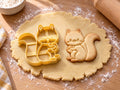 Butter-gelber Eichhörnchen-Ausstecher mit Prägung neben gebackenem Keks: Comic-Eichhörnchen hält eine Nuss, heller Holztisch