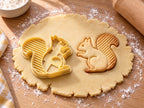 Butter-gelber Eichhörnchen-Ausstecher mit Prägung neben gebackenem Keks mit schräg gestreiftem Schwanz auf hellem Holz