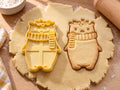 Butter-gelber Eisbär-Ausstecher mit Prägung neben gebackenem Keks mit Strickschal und Stechpalmenzweig auf hellem Holz