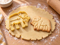 Butter-gelber Elefant-Ausstecher mit Prägung neben gebackenem Keks mit Stoßzähnen und faltigen Beinen auf hellem Holz