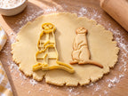 Butter-gelber Erdmännchen-Ausstecher mit Prägung neben gebackenem Keks: aufrecht stehendes Erdmännchen mit Augenringen auf hellem Holz