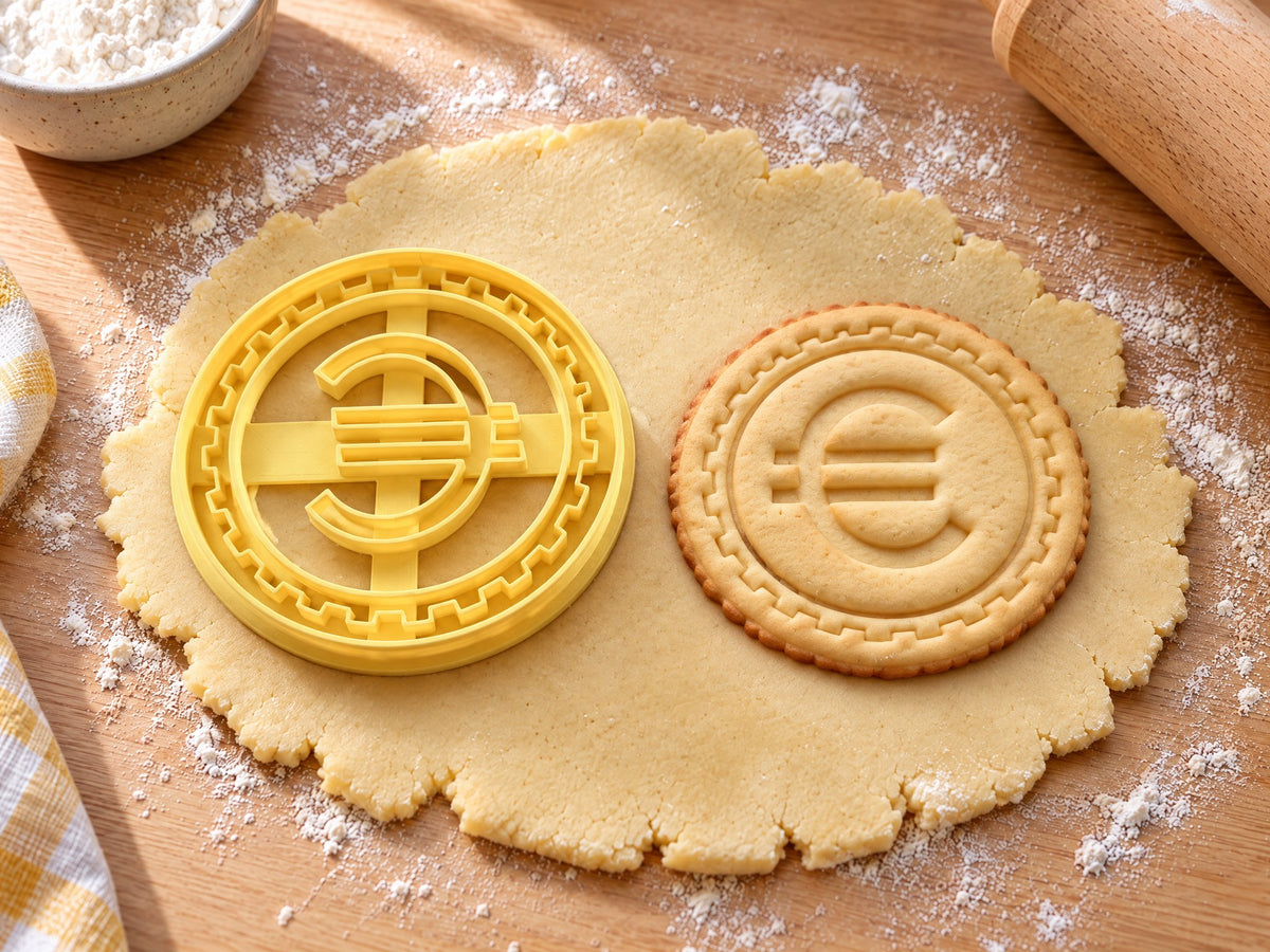 Butter-gelber Euro-Münzen-Ausstecher mit Prägung neben rundem Keks mit Eurozeichen und geriffeltem Rand auf hellem Holz