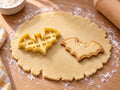 Butter-gelber Fledermaus-Ausstecher neben gebackenem Keks in glatter Silhouette mit Bogenflügeln und Spitzohren auf hellem Holz