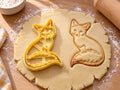 Butter-gelber Fuchs-Ausstecher mit Prägung neben gebackenem Keks: sitzender Fuchs mit fein gezeichnetem Fell und Rute, heller Holztisch