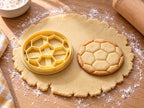 Butter-gelber Fußball-Ausstecher mit Prägung neben Ball-Keks mit kleinem Fünfeck und schmalen Randfeldern auf hellem Holz