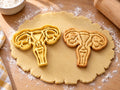 Butter-gelber Gebärmutter-Ausstecher mit Prägung neben gebackenem Keks mit Eileitern und Eierstöcken auf hellem Holz