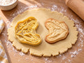 Butter-gelber Ausstecher mit Prägung als geöffnetes Gebiss neben gebackenem Keks mit oberer und unterer Zahnreihe auf hellem Holz