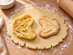 Butter-gelber Ausstecher mit Prägung als geöffnetes Gebiss neben gebackenem Keks mit oberer und unterer Zahnreihe auf hellem Holz