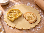 Butter-gelber Gehirn-Ausstecher mit Prägung neben gebackenem Keks mit Hirnwindungen, Kleinhirn und Hirnstamm auf hellem Holz