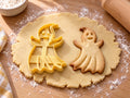 Butter-gelber Geist-Ausstecher mit Prägung neben lächelndem Gespenst-Keks mit Zipfelspitze und Faltenbahnen auf hellem Holz