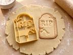 Butter-gelber Grabstein-Ausstecher mit Prägung neben Keks mit RIP-Schriftzug, Riss und abgeplatzter Ecke auf hellem Holz
