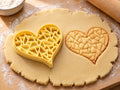 Butter-gelber Herz-Ausstecher mit Prägung neben gebackenem Keks in Herzform mit kantigem Mosaikmuster auf hellem Holz