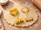 Butter-gelber Herzschlüssel-Ausstecher mit Prägung neben Keks mit herzförmigem Griff und verziertem Bart auf hellem Holz