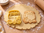 Butter-gelber Hexenkessel-Ausstecher mit Prägung neben Keks mit tropfendem Kessel und drei Kürbisgesichtern auf hellem Holz