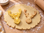 Butter-gelber Hirschkopf-Ausstecher mit Prägung neben gebackenem Keks mit verzweigtem Geweih und Fellzeichnung auf hellem Holz