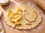 Butter-gelber Huhn-Ausstecher mit Prägung neben gebackenem Keks mit gefächerten Schwanzfedern und Halskrause auf hellem Holz
