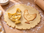 Butter-gelber Huhn-Ausstecher mit Prägung neben gebackenem Keks: rundliche Henne mit Flügelbogen und Streifenschwanz auf hellem Holz