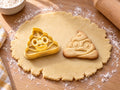 Butter-gelber Kackhaufen-Emoji-Ausstecher mit Prägung neben gebackenem Keks mit Windungen, Kulleraugen und Grinsen auf hellem Holz
