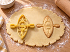 Butter-gelber Kajak-Ausstecher mit Prägung neben gebackenem Keks mit Sitzluke und quer liegendem Doppelpaddel auf hellem Holz