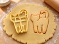 Butter-gelber Katzen-Ausstecher neben gebackenem Keks in Form einer stehenden Katze mit hochgebogenem Schwanz auf hellem Holz