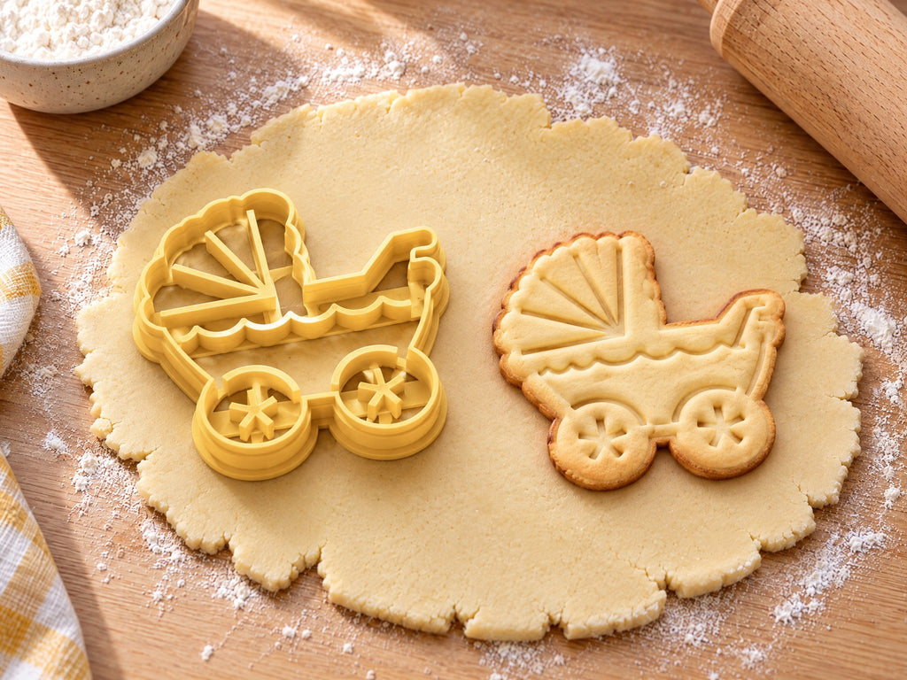 Butter-gelber Kinderwagen-Ausstecher mit Prägung neben Keks mit Faltverdeck, Wellenborte und Speichenrädern auf hellem Holz