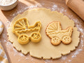 Butter-gelber Kinderwagen-Ausstecher mit Prägung neben Keks mit Faltverdeck, Wellenborte und Speichenrädern auf hellem Holz